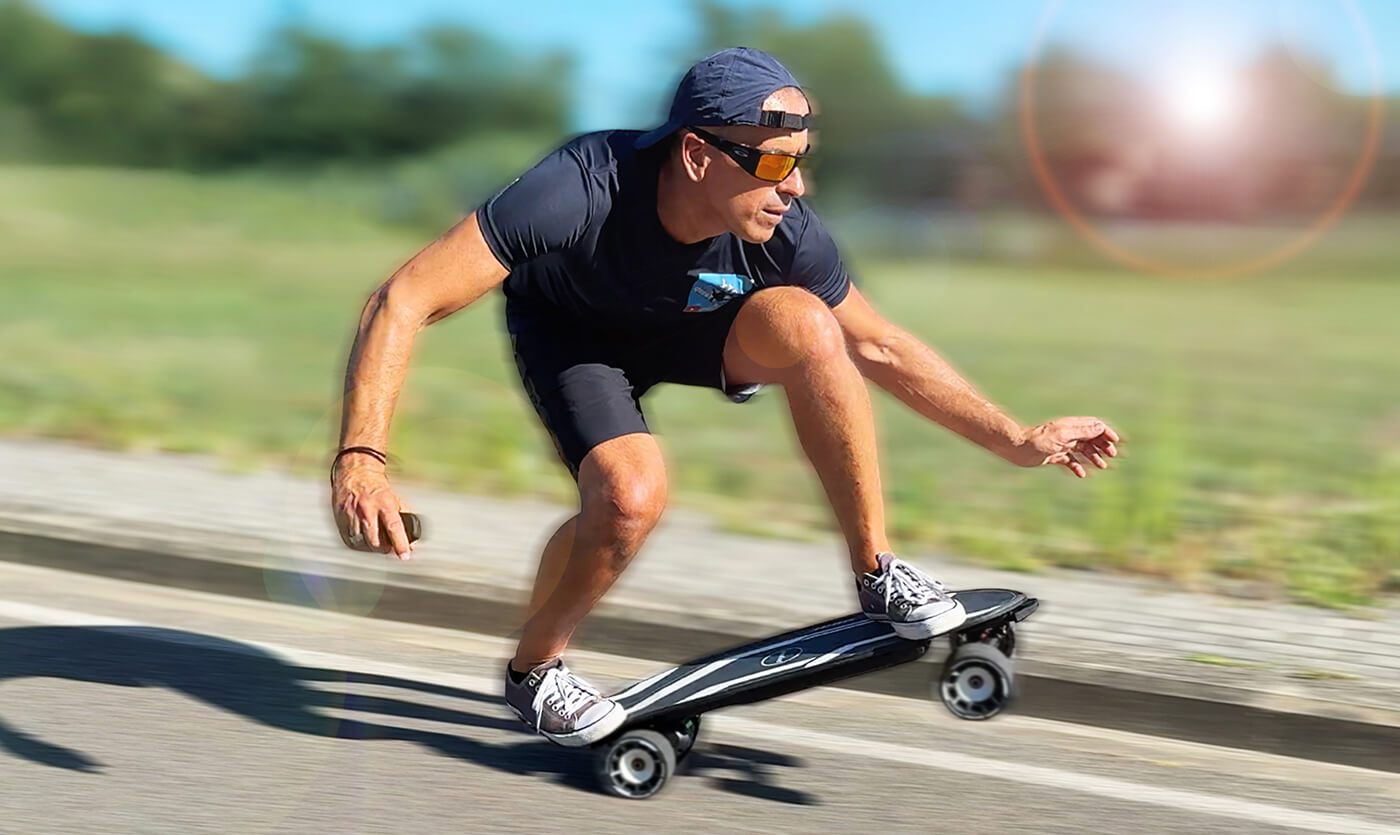 A man wearing sunglasses is riding an electric skateboard on the sidewalk.
